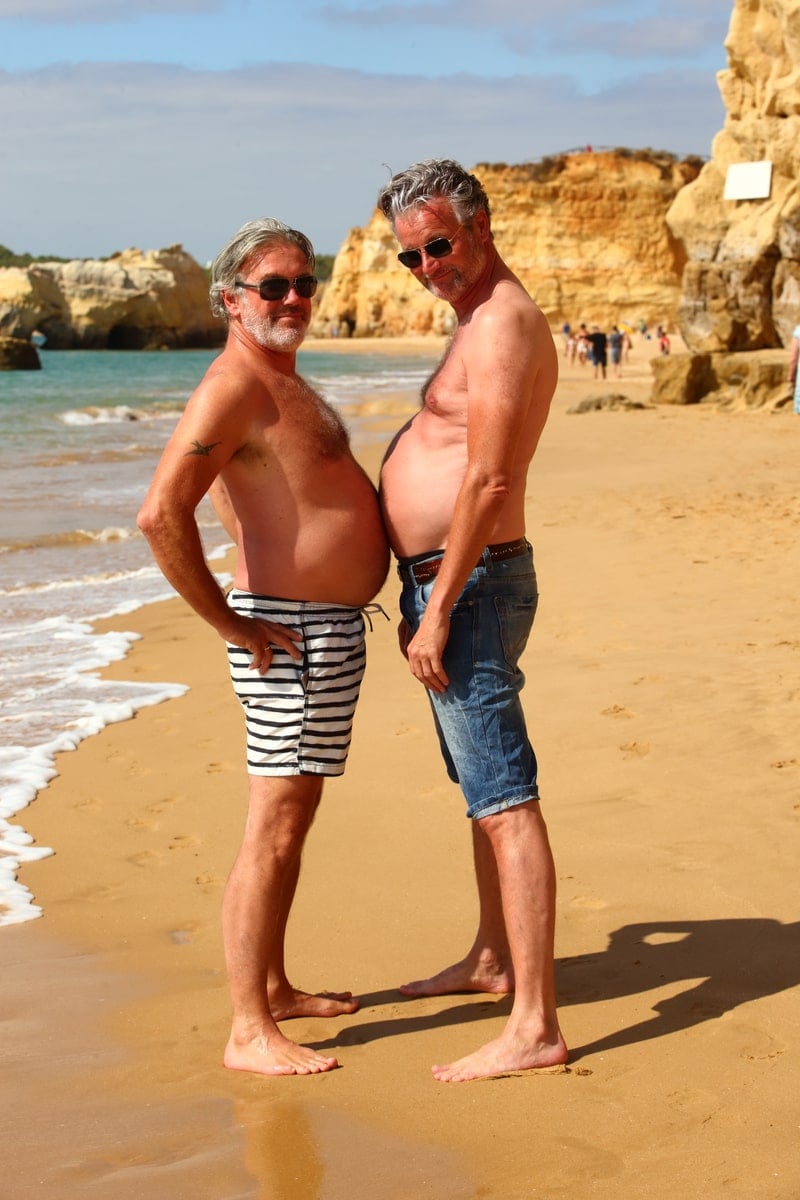 Zwei Männer demonstrieren während einer gemeinsamen schwulen Reise ihren Bierbauch.