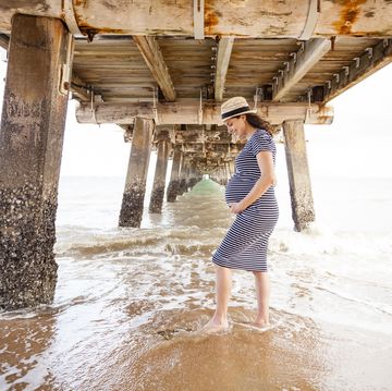 Eine schwangere Frau hält ihren Bauch am Strand