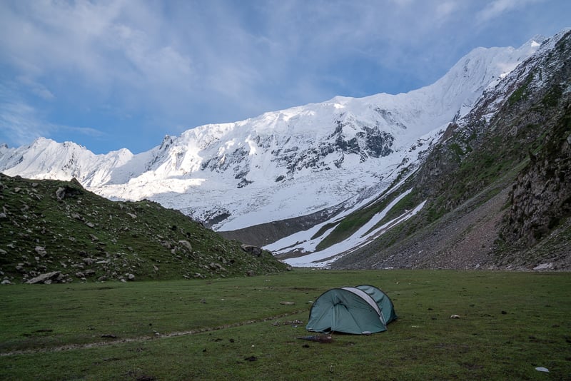 Grünes Zelt in einer Wiese unter einem massiven Berg, während sie in Pakistan reiste