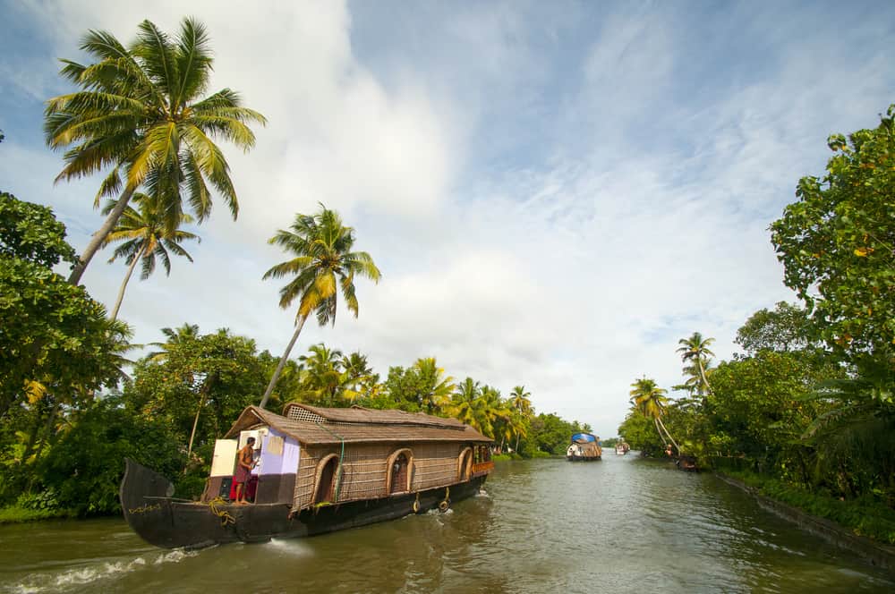 Ein Mann auf der Rückseite eines Bootshauss auf einem Kanal in Indien, der mit Palmen überwachsen ist