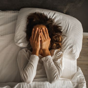 Die Frau in Depression bedeckte ihr Gesicht mit ihren Händen und weint im Bett mit einer melancholischen Stimmung und Problemen für psychische Gesundheit