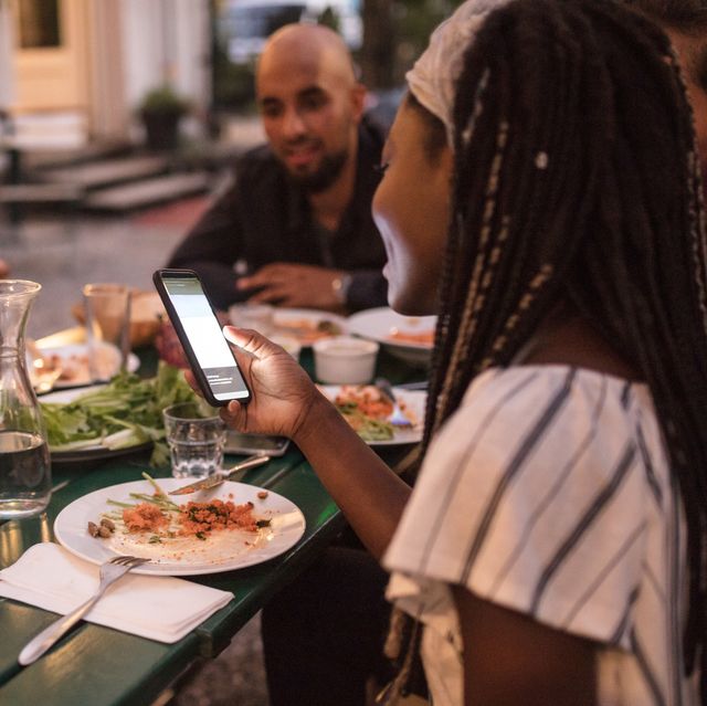 Eine junge Frau benutzt ein Smartphone während des Abendessens mit Freunden auf einer Party im Garten
